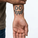 Tatuaggio semi-permanente INKON Creepy Smile applicato su un uomo – design 2 x 2 in (5x5cm), aspetto realistico dell'inchiostro, dura 10 giorni